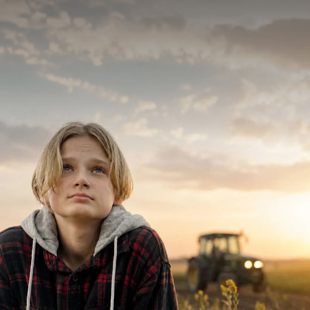 A Trailhead student in a flannel and hoodie looking up at a sunset sky, a tractor in the distance